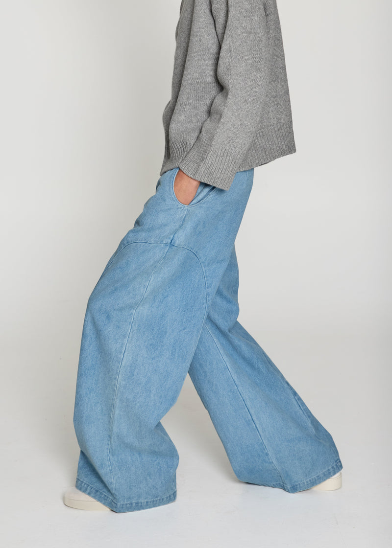 Person wearing light blue jeans and a gray sweater on a plain background